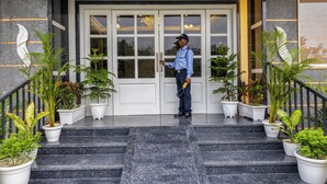 A security guard standing at the entrance of a building with a double door and a set of stairs leading up to it. - Yashobhoomi Hostel  (New Delhi)