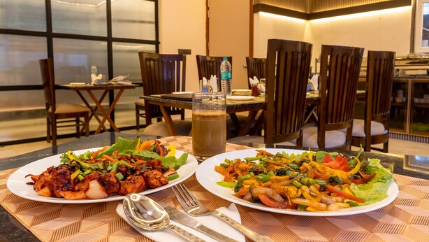 A restaurant with two plates of food on a table, a glass of beverage, and a fork and knife set. - Yashobhoomi Hostel  (New Delhi)