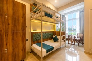 A bunk bed with a wooden headboard, a small table with chairs, and a view of the city through large windows. - Yashobhoomi Hostel (New Delhi)
