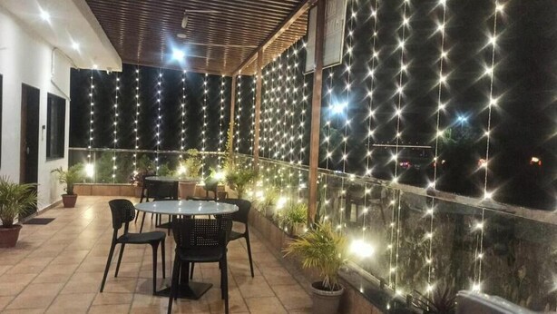 Un espace extérieur aménagé en terrasse, avec une table ronde et des chaises, des plantes en pot et des guirlandes lumineuses.