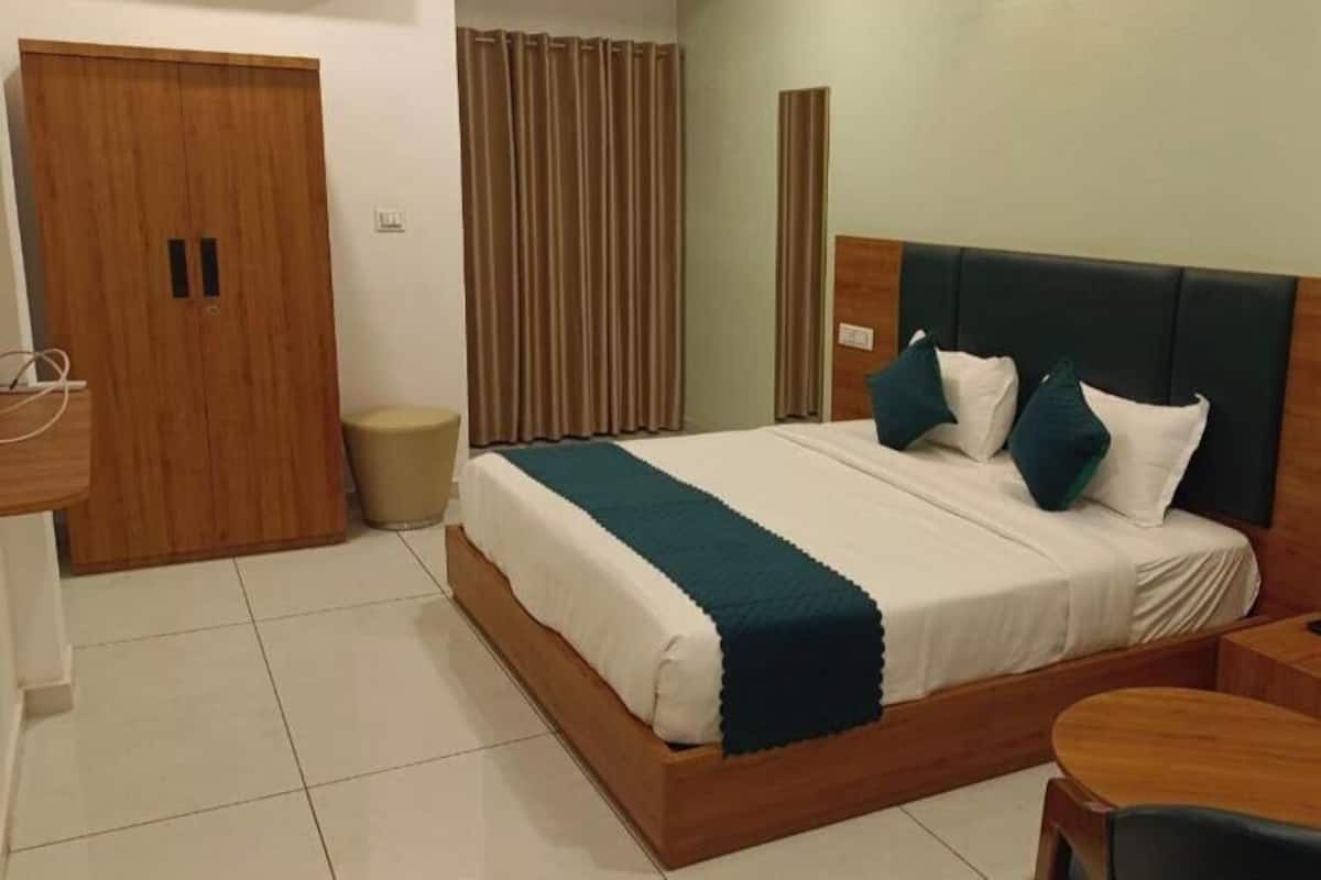 Una habitación de hotel con una cama de madera, una mesita de noche, una silla, un armario y una cortina.