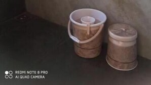 Une salle de bain avec un mur en marbre, un chauffe-eau fixé au-dessus du lavabo et deux seaux posés sur le sol.