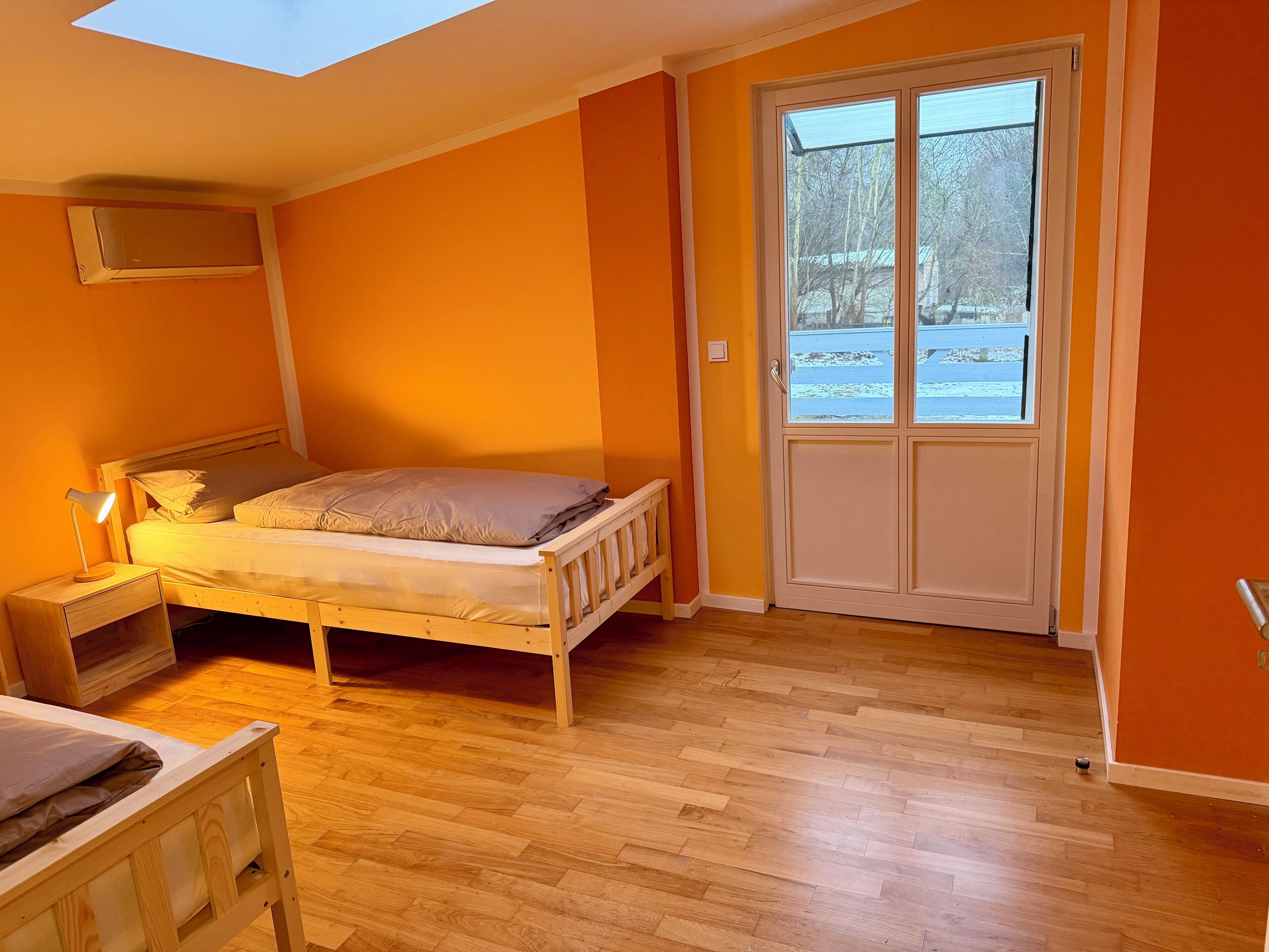A bedroom with a wooden bed, a nightstand, a desk, and a large window with a view of a snowy landscape.