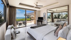 Una habitación de hotel moderna con una cama grande, un televisor, un balcón con vista al océano y un ventilador de techo.