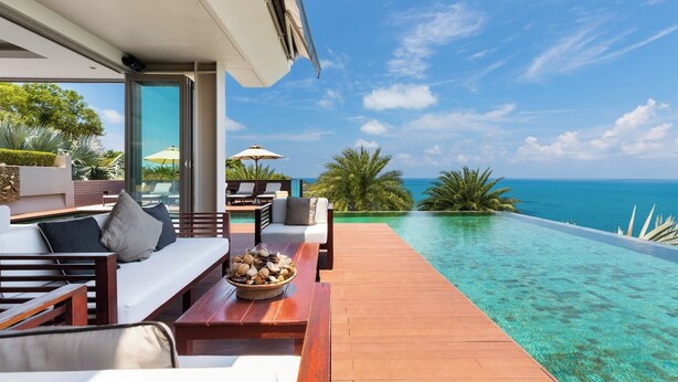 Un área de estar exterior lujosa con una terraza de madera, una piscina y vistas al océano.
