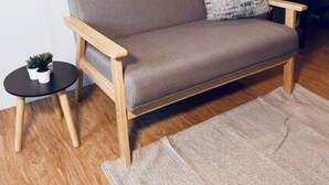 A grey sofa with wooden armrests, a small round side table with a plant, and a grey rug on a wooden floor. - Siqui Pods (Siquijor)