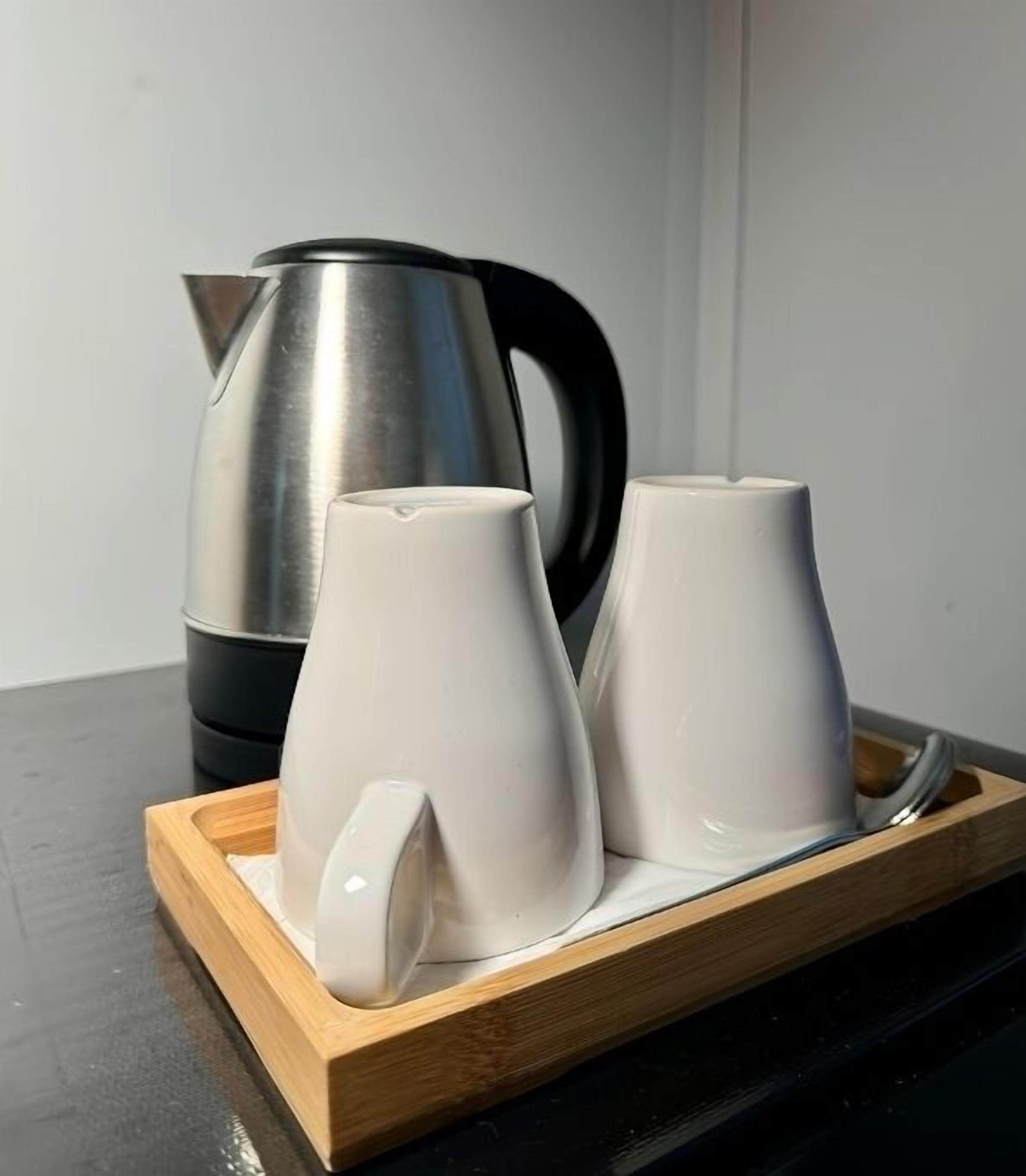 Una tetera de acero inoxidable y dos tazas de cerámica blanca sobre una bandeja de madera.