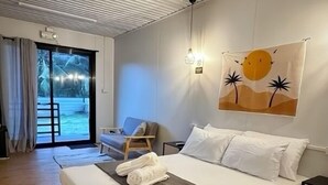 A modern bedroom with a large bed, a view of the outdoors through a sliding door, and a wall-mounted artwork. - Siqui Pods (Siquijor)