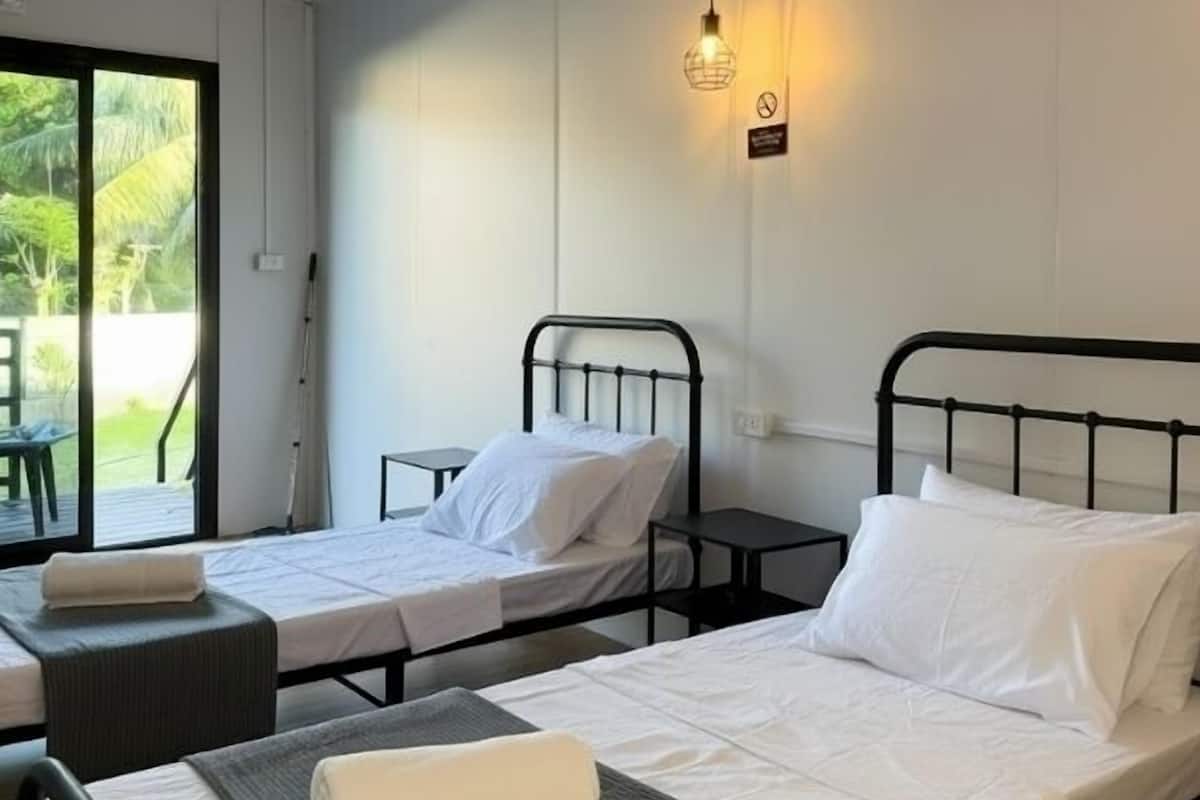 Una habitación con dos camas individuales, cada una con una almohada y una manta. Hay una mesita de noche al lado de cada cama, y una lámpara colgante arriba.