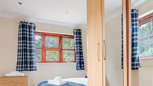 Una camera da letto con un letto, una cassettiera in legno, un armadio, una finestra con tende e un termosifone.