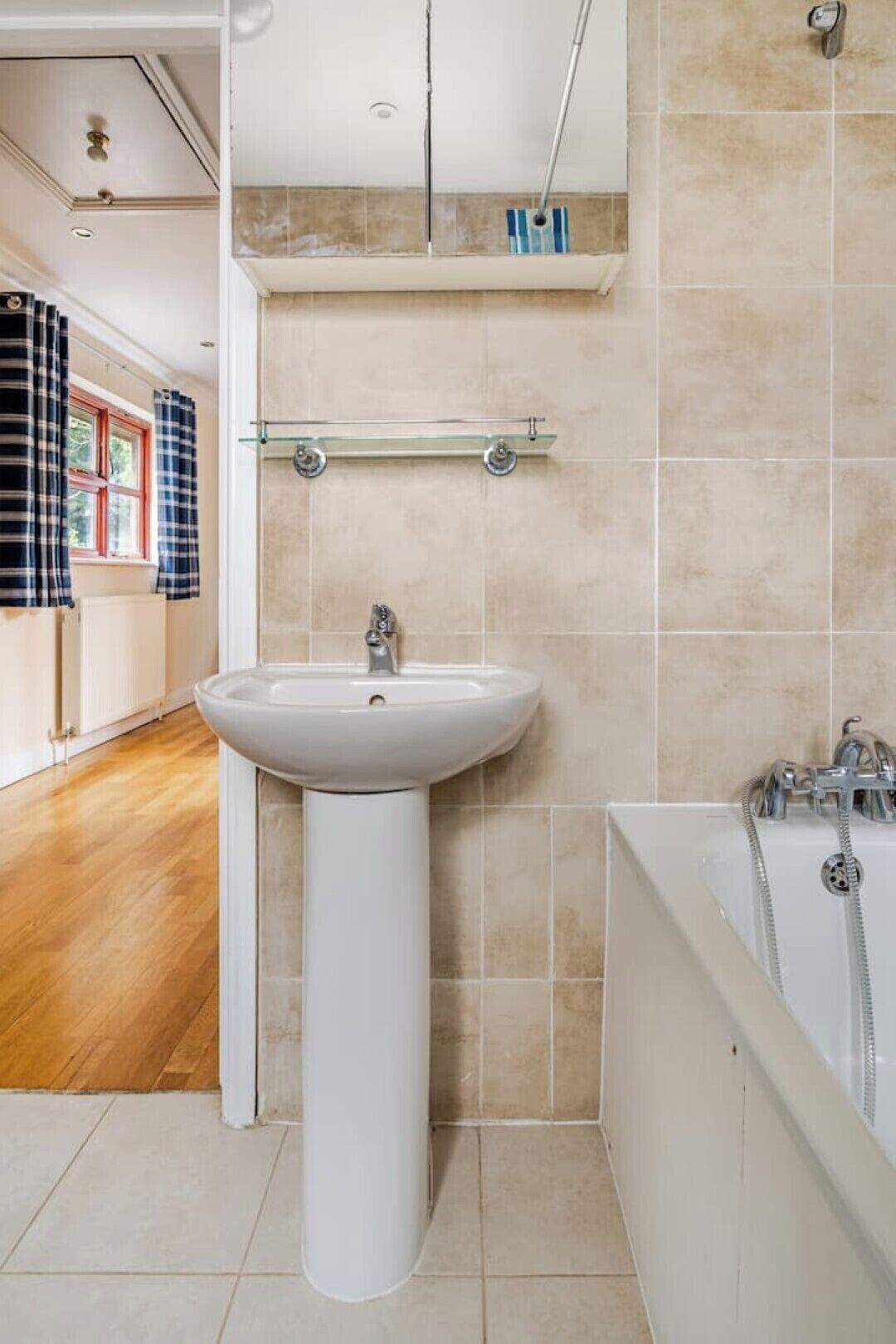 Une salle de bain moderne avec un lavabo sur colonne, une baignoire et une étagère en verre au-dessus du lavabo.