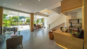 Un área de recepción moderna con un mostrador de madera, una escalera y una zona de estar con sillas y una mesa.