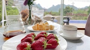Una mesa con fresas en un plato, una jarrón y una taza de café, con vistas a una montaña pintoresca.