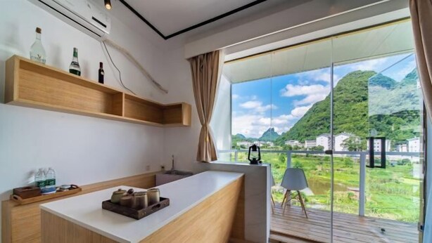 Una cocina moderna con una isla grande, estantes de madera y vistas a un paisaje montañoso a través de una puerta de cristal.