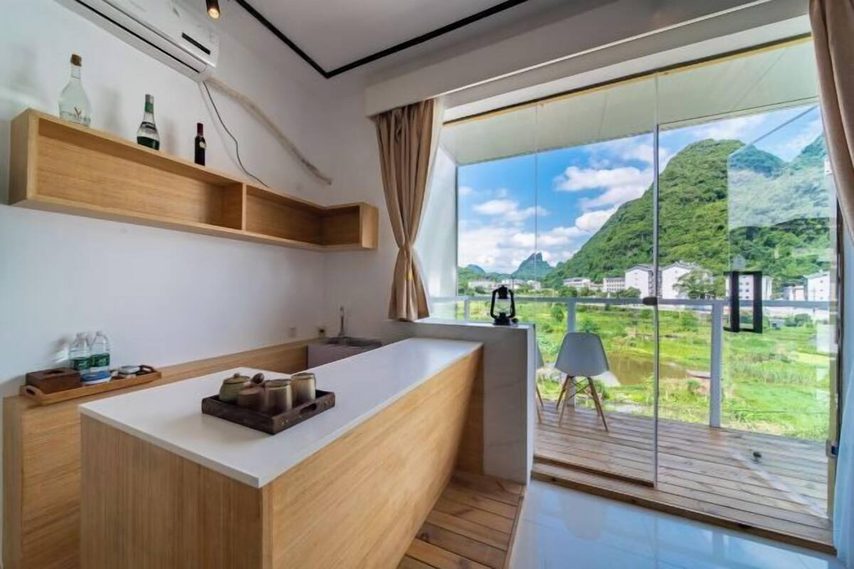 Una cocina moderna con una isla grande, estantes de madera y vistas a un paisaje montañoso a través de una puerta de cristal.