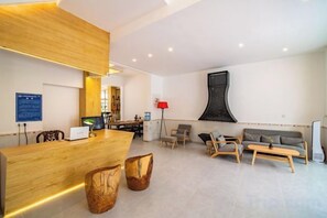 En hotellobby med en receptionsdisk i trä, en sittgrupp med soffor och fåtöljer samt ett stort, abstrakt konstverk på väggen.