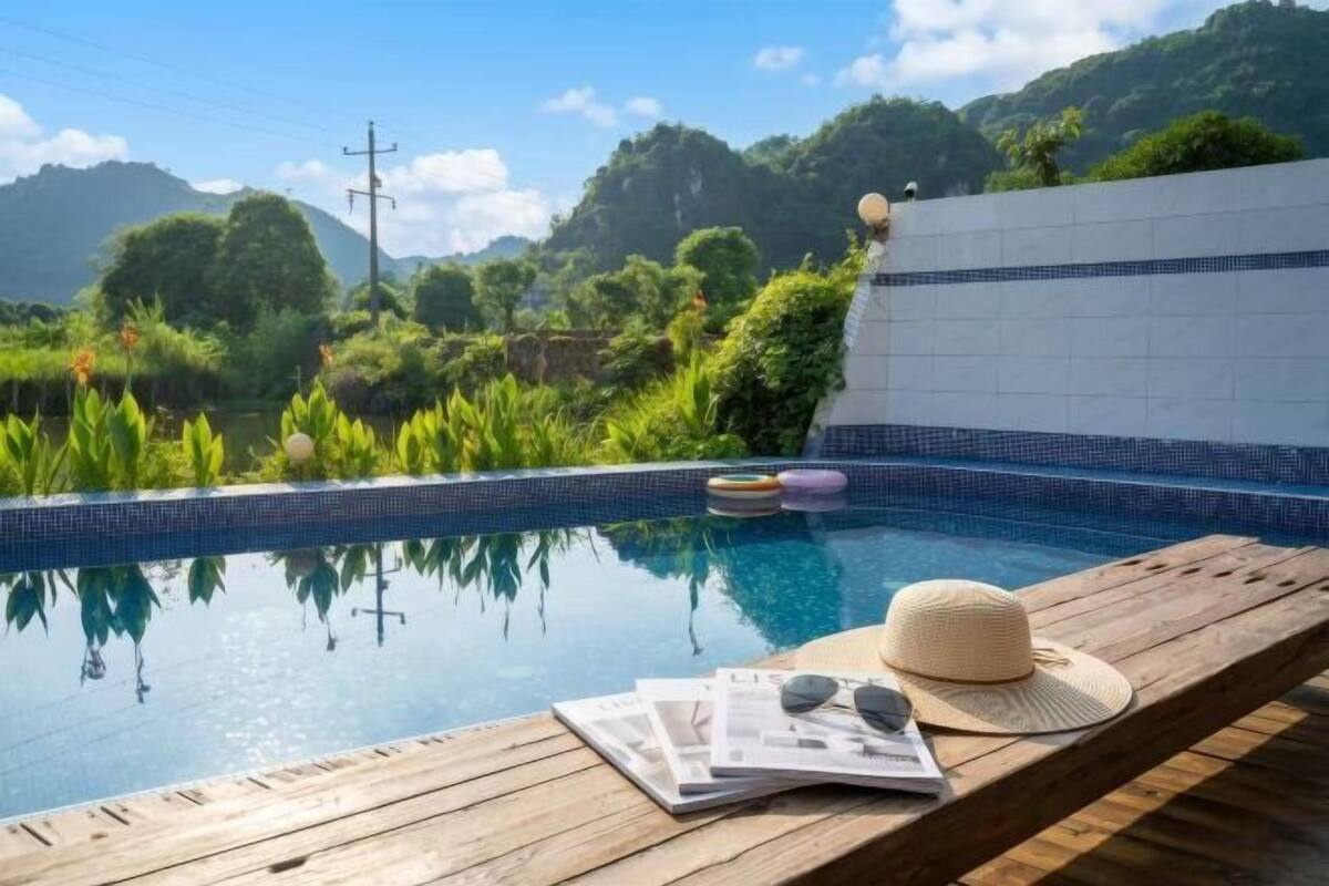 Una terraza de madera con piscina, un sombrero, gafas de sol y una revista.