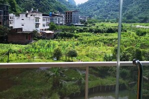 Vista desde un balcón con barandilla metálica, sobre un paisaje verde con edificios al fondo.