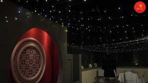 Un restaurante tenuemente iluminado con luces colgantes, un elemento decorativo rojo grande y mesas dispuestas para comer.