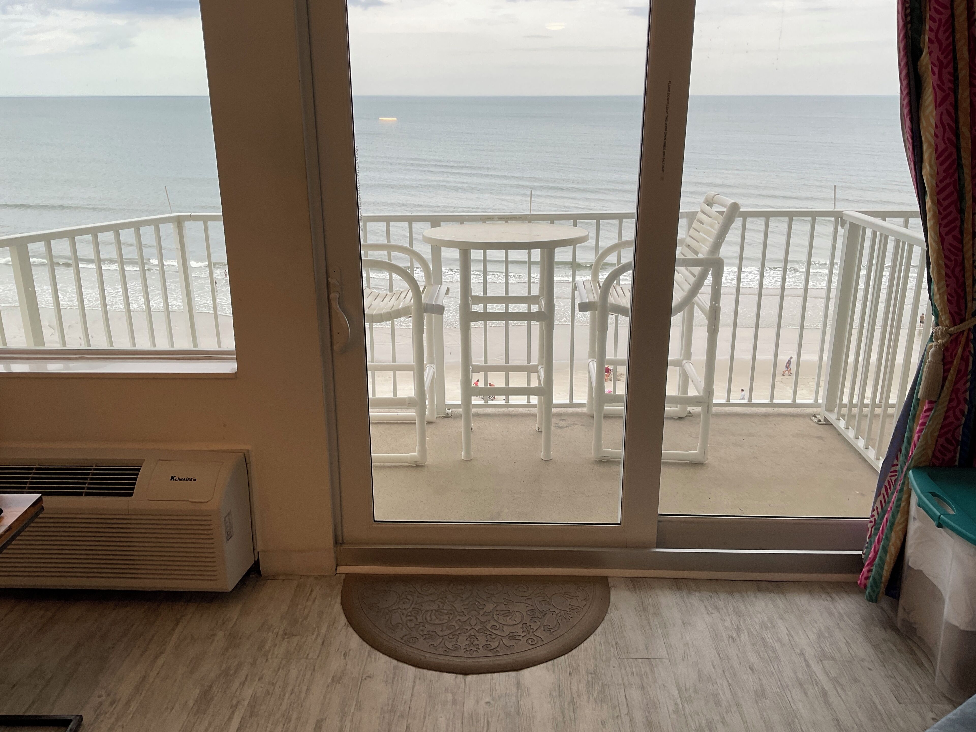 Una habitación con vista al mar, un balcón con sillas blancas y una pequeña mesa.
