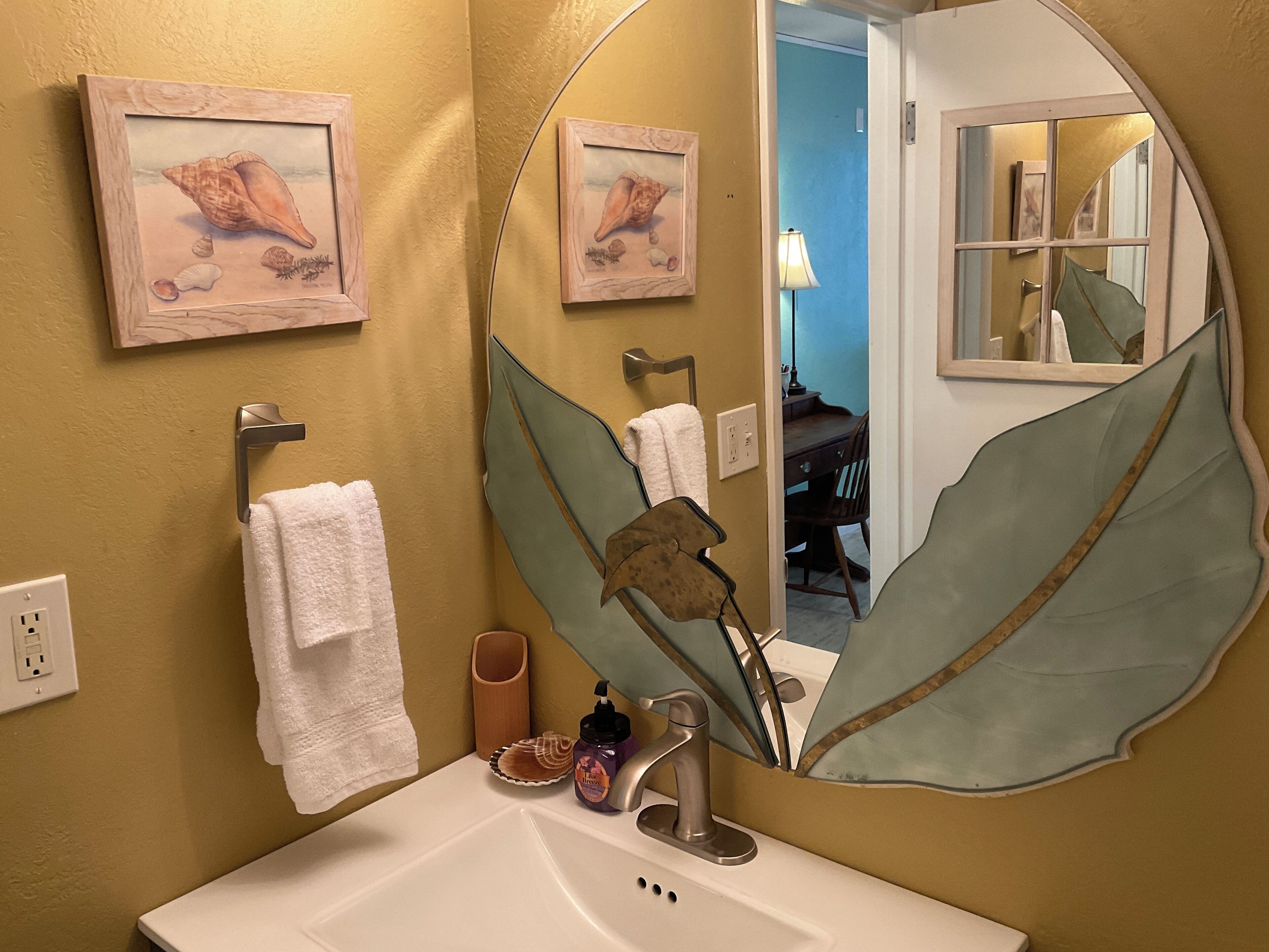 Une salle de bain avec un grand miroir, un lavabo, un porte-serviettes et des tableaux encadrés au mur.