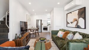 A modern living room with a green sofa, a dining table, and a kitchen in the background. - Refined Luxury Retreat with Premium Comforts. (Christchurch)