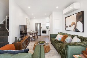 A modern living room with a green sofa, a dining table, and a kitchen in the background. - Refined Luxury Retreat with Premium Comforts. (Christchurch)