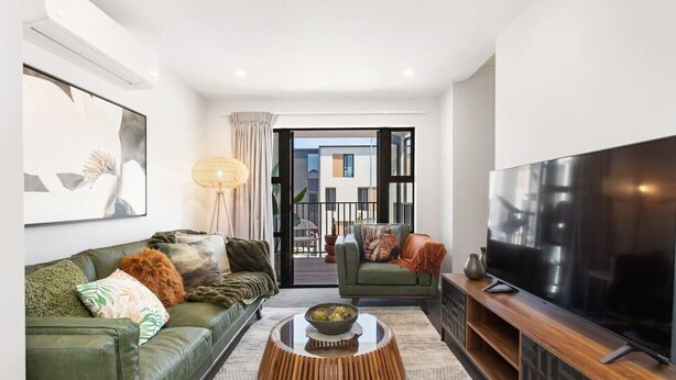 A modern living room with a green sofa, a wooden coffee table, a flat-screen TV, and a view to the outside. - Refined Luxury Retreat with Premium Comforts. (Christchurch)