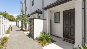 A row of modern, white two-story townhouses with dark front doors, a narrow driveway, and small front gardens. - Refined Luxury Retreat with Premium Comforts. (Christchurch)