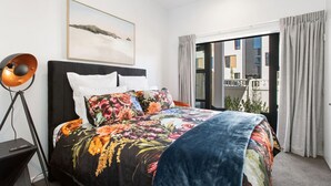 A bedroom with a large bed, a floor lamp, a painting on the wall, and a view through the window. - Refined Luxury Retreat with Premium Comforts. (Christchurch)