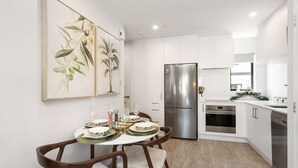 A modern kitchen with white cabinets, stainless steel appliances, and a dining area with a table set for four. - Refined Luxury Retreat with Premium Comforts. (Christchurch)