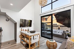 A modern kitchen with a large window, a dining area with a round table, and a cozy seating area with a wicker sofa and a patterned cushion. - Boutique Sophisticated One Bedroom Hideaway (Christchurch)