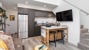 A compact kitchen with a modern design, featuring a built-in oven, a refrigerator, and a flat-screen TV mounted on the wall. - Boutique Sophisticated One Bedroom Hideaway (Christchurch)