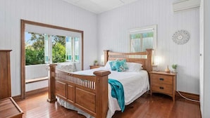 A bedroom with a wooden bed, a nightstand, a window with a view of greenery, and a ceiling fan. - 3br Queenslander, close to city, transport and shops (Cannon Hill)