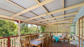 A covered outdoor deck with wooden furniture, a bed, and a small table with bottles. - 3br Queenslander, close to city, transport and shops (Cannon Hill)