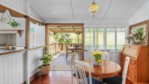 A dining area with a wooden table, white chairs, and a chandelier. There is a view of the outdoors through large windows. - 3br Queenslander, close to city, transport and shops (Cannon Hill)