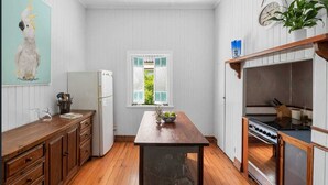 A kitchen with wooden cabinets, a white refrigerator, a wooden dining table, and a stove. - 3br Queenslander, close to city, transport and shops (Cannon Hill)
