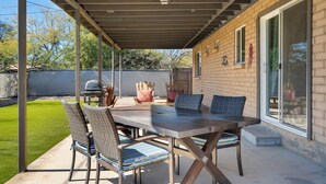 A covered patio with a table and chairs, a grill, and a view of the backyard. - Modern 3BR House w/ Fast WiFi & Large Backyard (Tucson)