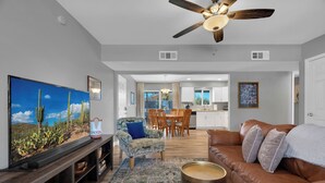 A modern living room with a flat-screen TV, a brown leather couch, a patterned armchair, and a ceiling fan. - Modern 3BR House w/ Fast WiFi & Large Backyard (Tucson)