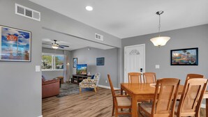 A dining area with a wooden table and chairs, a ceiling fan, and a painting on the wall. - Modern 3BR House w/ Fast WiFi & Large Backyard (Tucson)