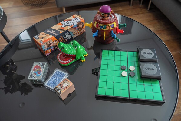 A table with a green board game, a Jenga box, a toy dinosaur, and a UNO box.