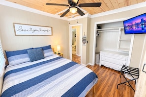 A bedroom with a bed, a ceiling fan, a TV, a wardrobe, and a bathroom visible through an open door.