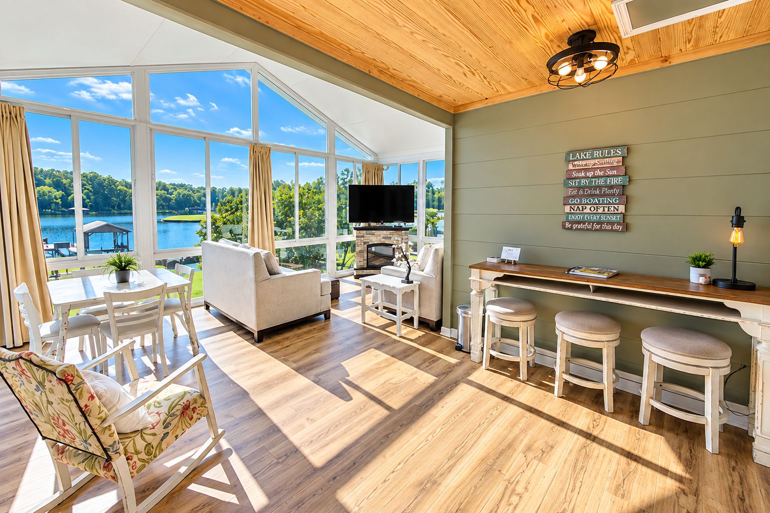 A spacious room with a large window overlooking a lake, a fireplace, a bar area, and a television.