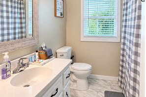 A bathroom with a sink, mirror, toilet, and window with blinds.