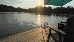 Eine Holzterrasse mit Stuhl und Sonnenschirm, mit Blick auf ruhiges Wasser und einem Sonnenuntergang im Hintergrund.