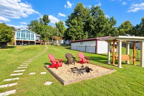 A backyard with a fire pit, red Adirondack chairs, and a gazebo.
