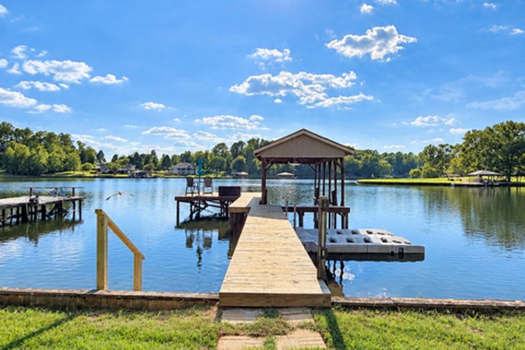 A wooden dock extending into a calm lake with a gazebo and seating area.