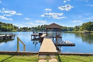 A wooden dock extending into a calm lake with a gazebo and seating area.