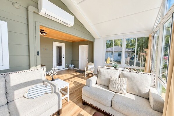 A sunlit living room with a sofa, a small table, and a view of the outdoors.