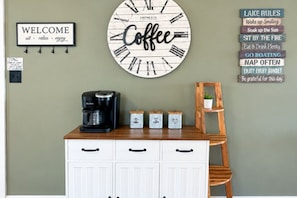 A kitchen area with a coffee-themed wall clock, a coffee maker, and a sign with motivational phrases. - Sunsets on Sinclair - Sleeps 6, Waterfront, Fire pit, Kayaks, Games + MORE! (Eatonton)